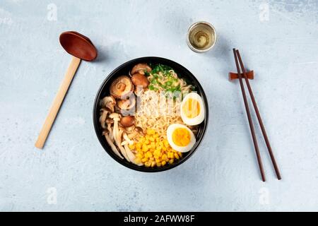 Ramen. Soupe de nouilles soba avec les oeufs, les champignons, et les légumes, tourné par le haut avec la traditionnelle cuillère en bois, des baguettes et du saké Banque D'Images