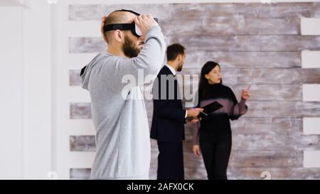 En réalité virtuelle à l'aide du casque dans nouvel appartement et femme parlant avec agent immobilier dans l'arrière-plan. Banque D'Images