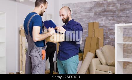 Le service de l'homme arrivant avec des cases et des documents à signer. Beau jeune couple le déménagement. Banque D'Images