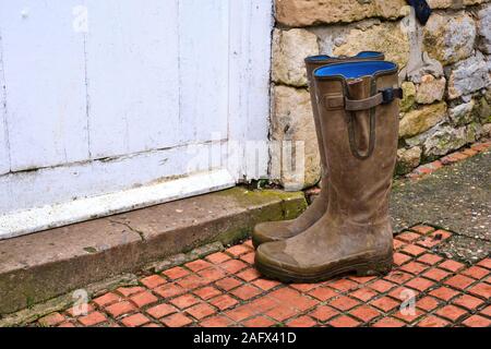 Vert bottes boueuses à l'extérieur de la porte d'une porte blanche à une maison de ferme en pierre. Couvre-bottes en caoutchouc bottes de gomme blucher boot Banque D'Images