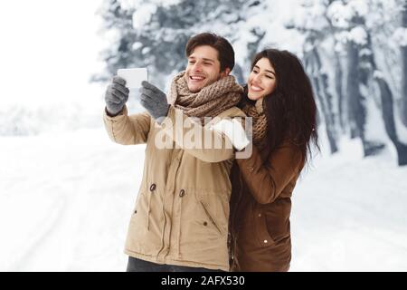 Couple aimant faire sur Selfies Phone Standing In Snowy Forest Banque D'Images