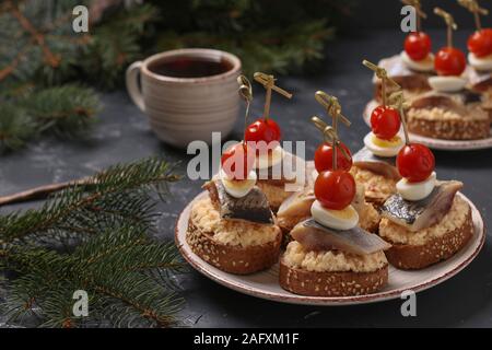 Des canapés avec hareng salé, fromage, œufs de caille et tomates cerise sur le seigle croûtons sur fond sombre, l'orientation horizontale Banque D'Images