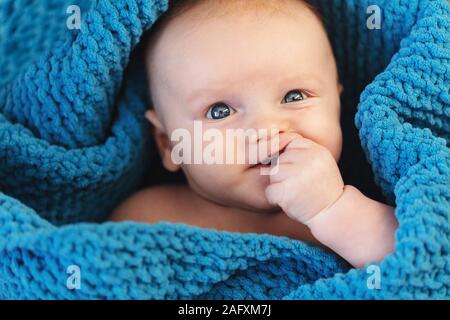 Un mignon petit garçon enveloppé dans une couverture bleue à la recherche à l'appareil photo Banque D'Images