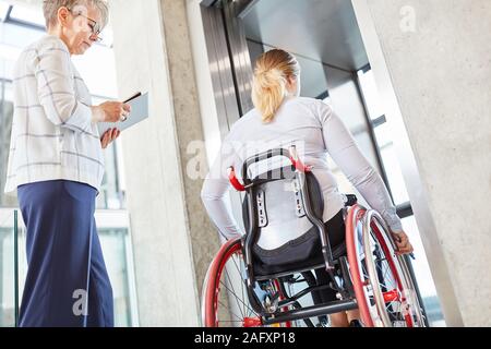 Femme handicapée dans un fauteuil roulant et un collègue dans l'ascenseur dans le bureau d'affaires Banque D'Images