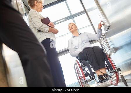 Mobilité jeune femme dans un fauteuil roulant appuie sur un bouton dans l'ascenseur au bureau Banque D'Images