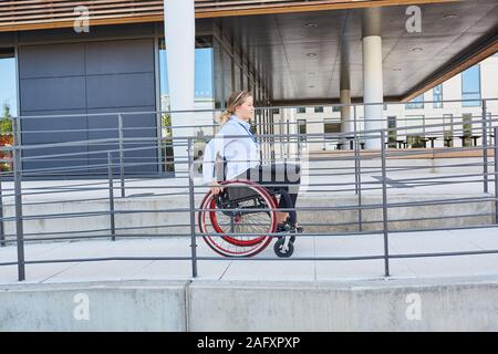 Femme handicapée dans un fauteuil roulant sur une rampe à l'office d'affaires Banque D'Images