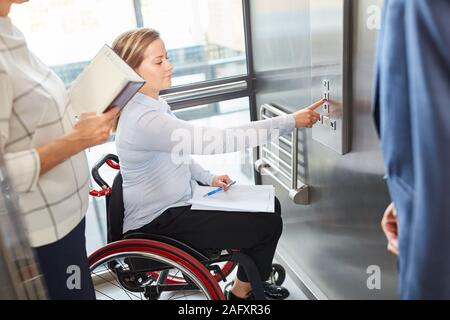 Jeune femme dans un fauteuil roulant appuie sur un bouton dans l'ascenseur dans l'entreprise Banque D'Images