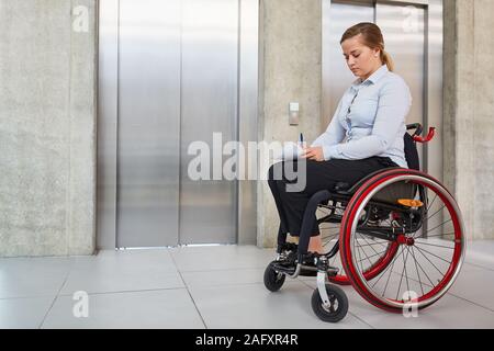 Jeune femme dans un fauteuil roulant dans une porte d'ascenseur dans l'entreprise comme un concept d'inclusion Banque D'Images