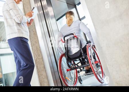 Femme dans un fauteuil roulant qui voyage avec l'ascenseur de l'entreprise La société Banque D'Images