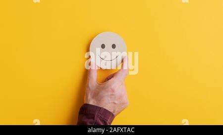 Placer une main mâle rond coupé en bois avec le visage souriant sur fond jaune. Avec l'exemplaire de l'espace. Banque D'Images