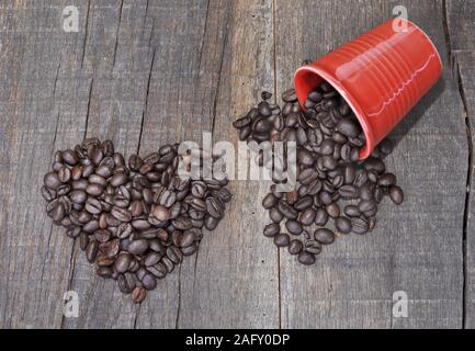 En forme de coeur dans les grains de café et une tasse pleine de rouge renversé sur une planche de haricots rustique Banque D'Images