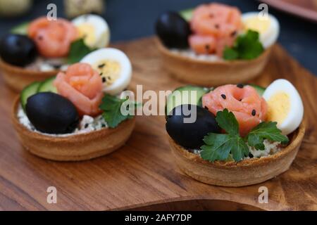 Maison de vacances tartelettes avec du fromage, du saumon, olives noires, œufs de caille et des concombres sur planche de bois sur fond sombre, l'orientation horizontale Banque D'Images