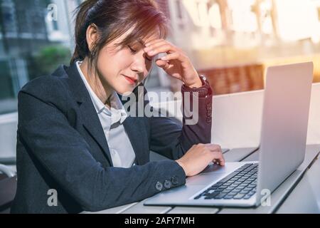 Asian business woman feeling bad migraine lors de la lecture de mauvaises nouvelles rapport d'entreprise échouer from laptop email. Banque D'Images