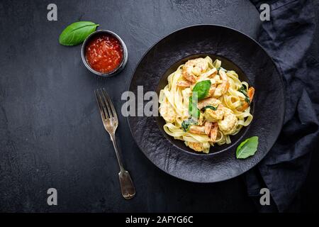 Les pâtes italiennes Les pâtes dans une sauce crémeuse aux crevettes sur une plaque noire, vue du dessus Banque D'Images