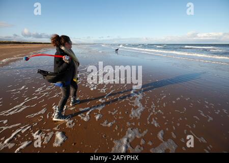 Une femme lance un ballon pour un chien noir du Labrador sur la plage de Brancaster à Norfolk. Banque D'Images
