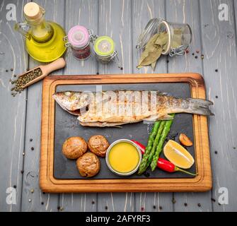 Bar grillé les poissons avec les pommes de terre et les légumes sur fond de bois Banque D'Images