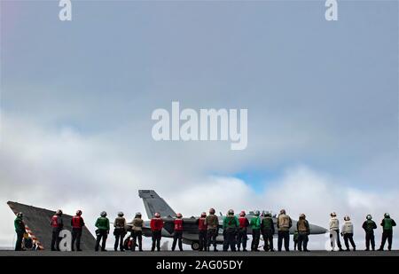 Les marins de la Marine américaine watch un E/A-18 Growler d'avions de chasse, attribué à l'électronique de Loups gris Attack Squadron 142, avant qu'il lance depuis la cabine de pilotage de la classe Nimitz porte-avions USS Theodore Roosevelt au cours des opérations de formation, le 16 décembre 2019 dans l'océan Pacifique. Banque D'Images