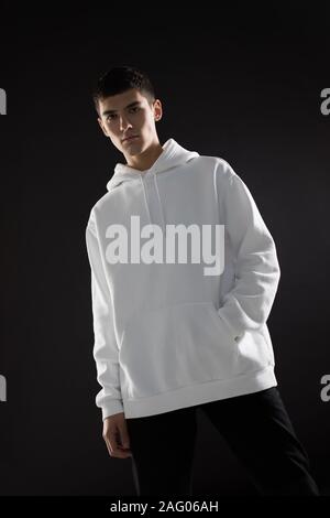 Jeune homme dans un pull à capuche blanc sur fond noir. Mock-up. Banque D'Images