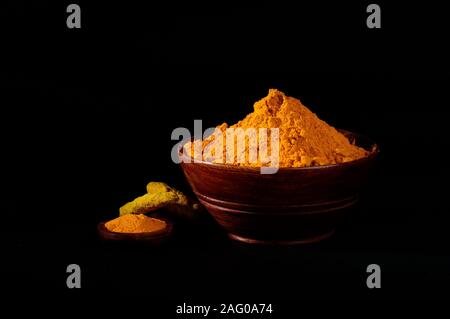 Poudre de curcuma et de racines ou des bâtons dans bol en bois sur fond noir Banque D'Images