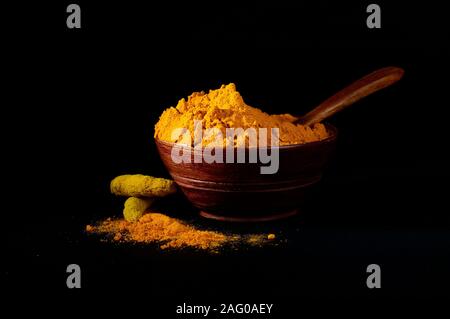 Poudre de curcuma et de racines ou des bâtons dans bol en bois sur fond noir Banque D'Images