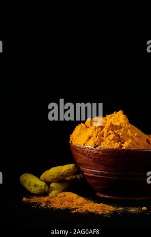 Poudre de curcuma et de racines ou des bâtons dans bol en bois sur fond noir Banque D'Images