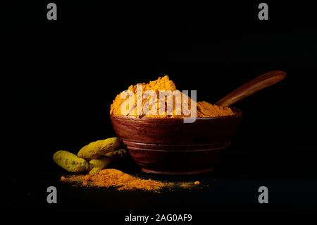 Poudre de curcuma et de racines ou des bâtons dans bol en bois sur fond noir Banque D'Images