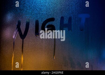 Le mot NUIT manuscrit par le doigt sur la nuit humide fenêtre gros plan en verre avec arrière-plan flou Banque D'Images