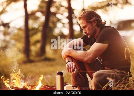 Profitant de la pause. Man in Black shirt près du feu de camp dans la forêt, à son temps de fin de semaine Banque D'Images