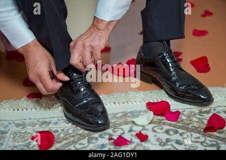 Homme portant un costume de mettre ses chaussures brunes. Les mains et le service de close-up. Vue rapprochée de l'homme Magnifique laçage mains chaussures élégantes. jour du mariage le marié. Banque D'Images