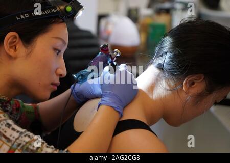 Middletown, CT / USA - 7 décembre 2019 : artiste de tatouage se concentre en traçant un dessin de tatouage floral sur l'arrière du cou du client Banque D'Images