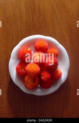 Fraises irlandaise (Arbutus unedo) servi sur un plat sur une table en bois. Banque D'Images