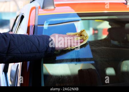 L'homme après le lavage du pare-brise de ses lingettes voiture orange avec un chiffon jaune au lave-auto. La main de voiture et fenêtre. Banque D'Images