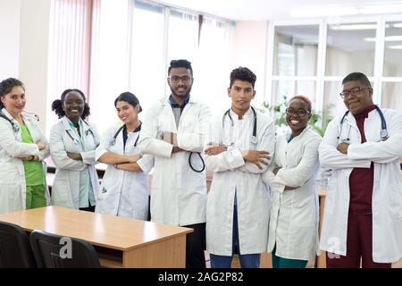 Les étudiants en médecine, médecins, race mixte. Une équipe de jeunes gens en blouse blanche posant dans le couloir de l'hôpital Banque D'Images