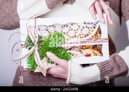 Frohe Weihnachten veut dire Joyeux Noël en allemand, l'inscription sur le ruban. Female hands holding Christmas gift box avec des biscuits sucrés faits maison Banque D'Images