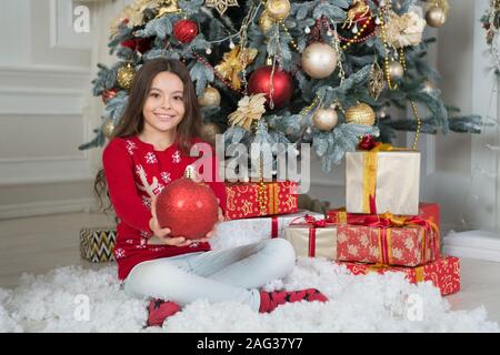 Décor d'attributs de Noël. Mes vacances d'hiver parfait. Petite fille près de l'arbre de Noël. Enfant célébrer Noël à la maison. Traditions d'hiver. Boutique cadeaux concept. Porter le chandail de Noël pour enfants adorables. Banque D'Images