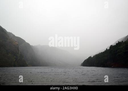 Prise de vue en niveaux de gris d'un lac entouré de collines sous le ciel gris brumeux en arrière-plan Banque D'Images