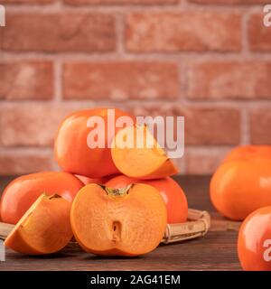 De belles tranches de patates douce kaki Kaki foncé sur table en bois avec mur de brique rouge, nouvelle année lunaire chinoise concept design fruits, Close up Banque D'Images