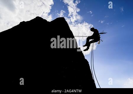 Une silhouette spectaculaire d'un grimpeur qui descend un mur de rochers. Grimpeur de roche avec un rappel de corde vers le bas Banque D'Images