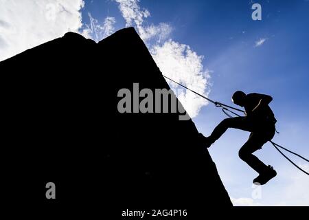 Une silhouette spectaculaire d'un grimpeur qui descend un mur de rochers. Grimpeur de roche avec un rappel de corde vers le bas Banque D'Images