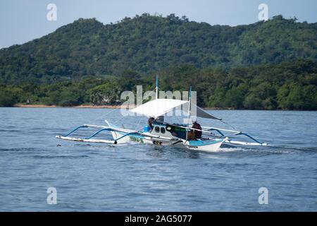 Un petit bateau en bois traditionnel banca avec deux personnes à bord à Coron Palawan Philippines,,. Banque D'Images