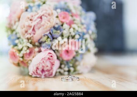 Gros plan d'un mariage anneaux près d'un bouquet de fleurs avec un arrière-plan flou Banque D'Images