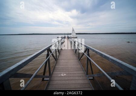 Photo en niveaux de gris d'un quai en bois dans l'océan avec un seul bateau sous le ciel nuageux Banque D'Images