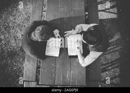 Vue aérienne de deux mâles assis dans le parc et la lecture de la bible en noir et blanc Banque D'Images