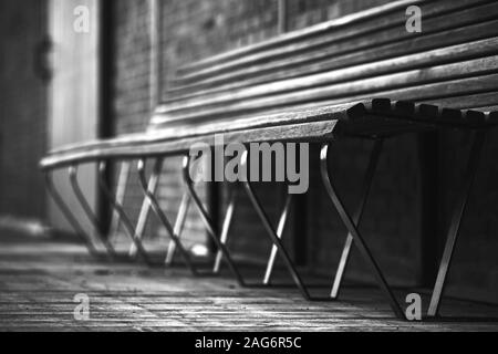 Prise de vue en bas angle en niveaux de gris d'un banc en bois dans le dans une zone urbaine Banque D'Images