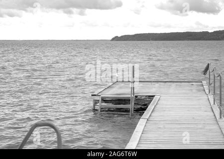 Prise de vue en niveaux de gris d'un quai en bois près de la belle mer sous le ciel nuageux Banque D'Images