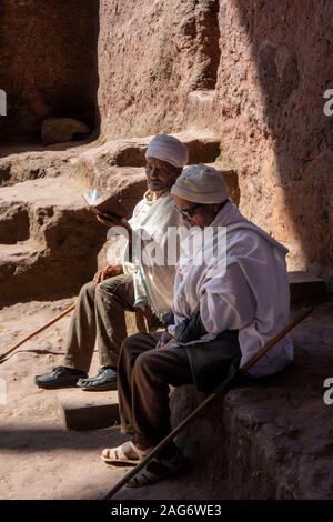 L'Éthiopie, région d'Amhara, Lalibela, Bet Maryam cour intérieure de l'Église, deux prêtres lecture evangile dans sunshine Banque D'Images