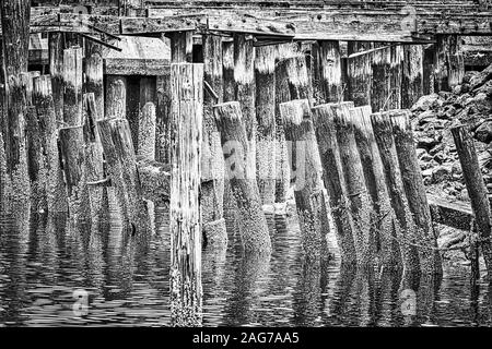 Cliché en échelle de gris de billes de bois au milieu de la rivière près de la jetée en bois Banque D'Images