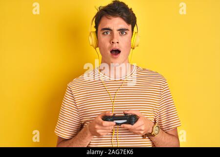 Adolescents jouant des jeux vidéo à l'aide de la manette de jeu sur fond jaune isolé peur sous le choc avec un visage surpris, effrayé et excité avec crainte expr Banque D'Images