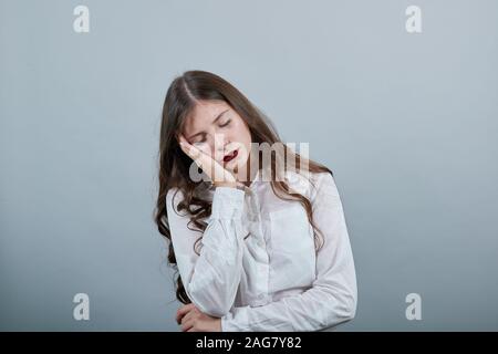 Femme endormie en chemise blanche en gardant la main sur la joue, faisant des gestes du sommeil Banque D'Images