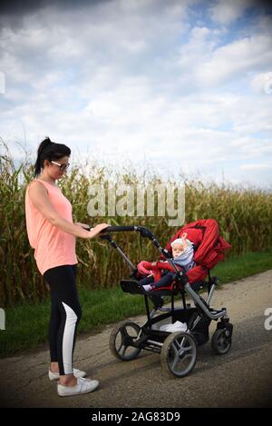 Adorable baby girl à l'extérieur en rouge poussette dans les champs avec sa mère. Sucette nouveau-né avec. Banque D'Images